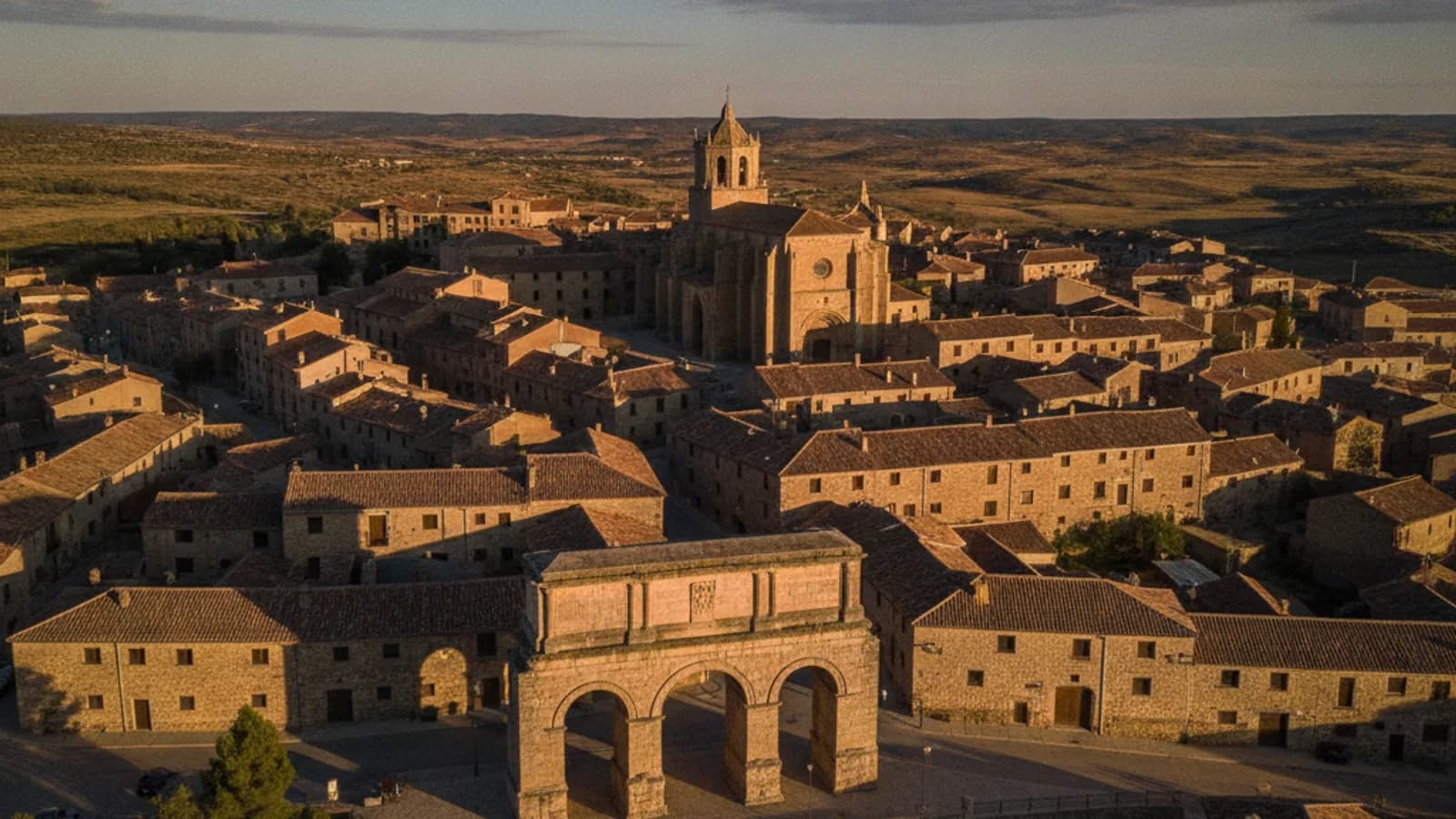 Vista aérea de Medinaceli con su emblemático arco romano, la colegiata y las casas de piedra bajo un cielo azul