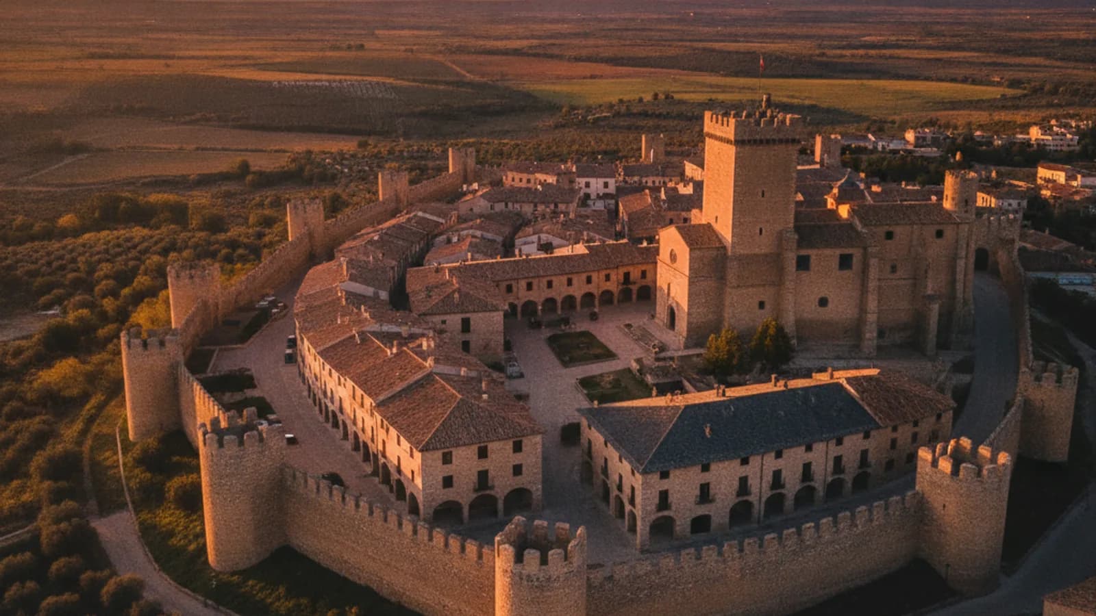 Vista aérea de Pedraza al atardecer, con sus casas de piedra y la torre del castillo iluminadas por la luz dorada, destacando la muralla y la Plaza Mayor.