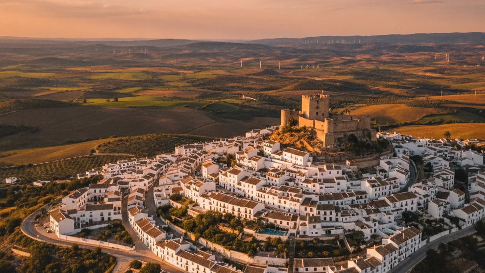 Vista panorámica de Vejer de la Frontera con sus casas blancas encaladas y el castillo al atardecer, con la campiña gaditana al fondo.